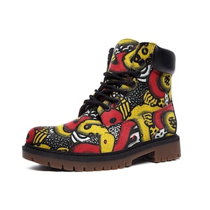 May include: A colorful combat boot featuring a vibrant pattern of red, yellow, black, and white abstract shapes. The boot has a black collar, black laces, and a brown sole. The design is eye-catching and bold.