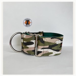 May include: A wide martingale dog collar featuring a camouflage pattern in shades of olive green, tan, and black. The collar includes heavy-duty silver-toned metal hardware, including a large D-ring and slides, with a dark green inner lining.