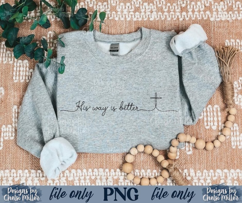 May include: A light gray sweatshirt with the text "His way is better" and a cross design. The long-sleeved crew neck top has rolled-up cuffs. The image also includes a string of wooden beads and greenery.