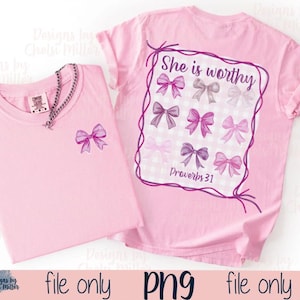Pu&ograve; includere: Due magliette rosa chiaro. Una maglietta ha una piccola grafica a fiocco sul davanti. L'altra maglietta ha un disegno sul retro con la scritta "She is worthy" e grafiche a fiocco. &Egrave; presente anche il testo "Proverbs 31".
