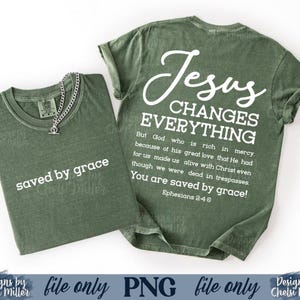 May include: Two olive green t-shirts with white text. One shirt says "saved by grace" and the other says "Jesus Changes Everything" with a Bible verse. A silver chain necklace is on the first shirt.
