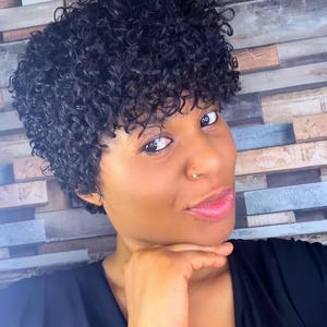 May include: A short, black wig featuring tight, defined curls and a textured, voluminous style. The hair is cropped close to the head with a rounded shape, showcasing a dense pattern of small, springy coils that frame the face evenly.