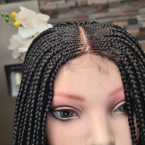Puede incluir: Peluca negra trenzada con frontal de encaje. La peluca está peinada en trenzas pequeñas y tiene una línea de cabello natural.