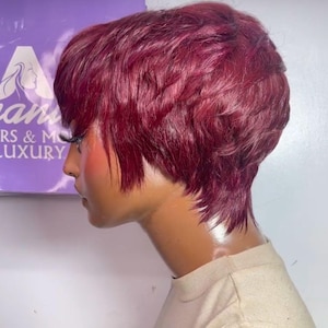 Peut inclure: Une perruque courte de couleur bordeaux avec un style dégradé et effilé. La perruque est coiffée avec une raie sur le côté et une frange droite.