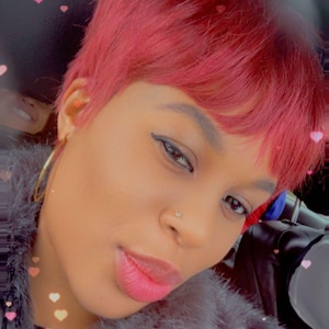 Peut inclure: Une personne aux cheveux courts et rouge vif et un piercing au nez. Elle porte des créoles dorées et un manteau de fausse fourrure grise. Des autocollants roses en forme de cœur sont éparpillés autour de l'image.