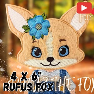 May include: A 4x6 inch embroidered patch of a fox wearing a denim dress and a blue flower. The fox has brown fur, blue eyes, and a pink nose. The text "Rufus Fox" is below the fox.