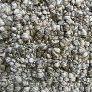 May include: Close-up of a grey and green woven rug with a textured, bumpy surface. The rug has a white border.