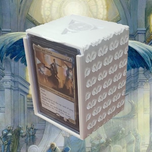 May include: White cube-shaped card storage box with a decorative pattern on the front and a Magic: The Gathering card visible inside. The card is "Eternal Witness" from the "Shards of Alara" set.