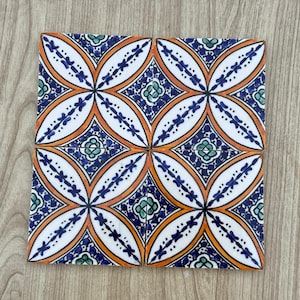 May include: Four square ceramic tiles with a repeating floral pattern. The design features white, orange, blue, and green colors. The tiles are arranged in a square, showcasing the symmetrical pattern. The tiles are likely for home decor or a craft project.