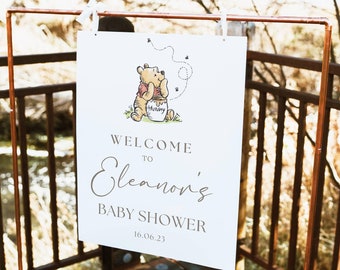 Puede incluir: Un cartel blanco con una ilustración de Winnie de Pooh y el texto "Bienvenido al baby shower de Eleanor 16.06.23".