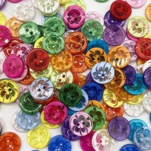 Könnte beinhalten: Sortiment an bunten Plastikknöpfen mit Blumenmustern. Die Knöpfe sind in verschiedenen Größen und Formen, jeweils mit zwei Löchern.