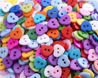 May include: A large assortment of heart-shaped buttons in various colours, including red, blue, green, purple, pink, yellow, and white. The buttons have two holes each.