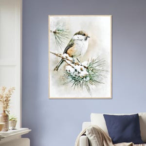May include: A framed watercolor print of a small bird perched on a snow-covered pine branch. The bird has a brown head, white chest, and tan wings. The artwork has a soft, muted color palette with a light brown wooden frame. The overall theme is nature and wildlife.