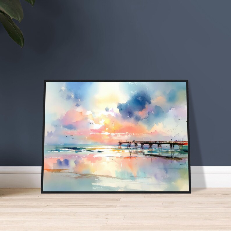 Puede incluir: Una pintura en acuarela enmarcada que representa una escena costera con un muelle de madera que se extiende hacia el oc&eacute;ano bajo un cielo vibrante lleno de nubes suaves en tonos rosa, naranja, amarillo y azul, reflej&aacute;ndose en la arena mojada.