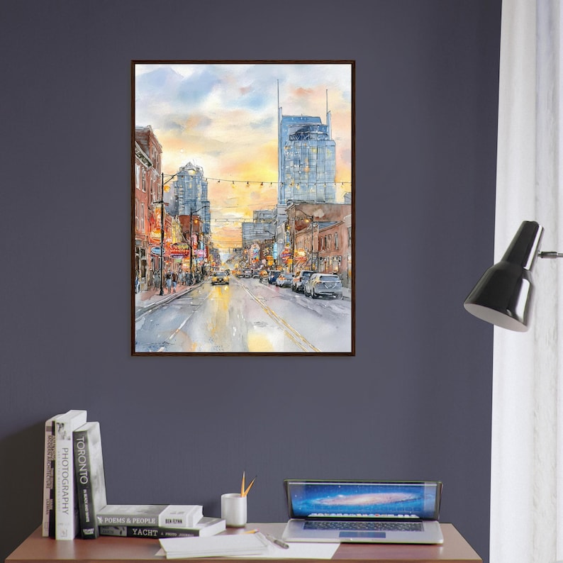 May include: A framed watercolor painting depicting a city street scene at sunset. The artwork features tall buildings, glowing streetlights, and vehicles on a wet road, with a warm yellow and orange sky reflecting on the pavement below.