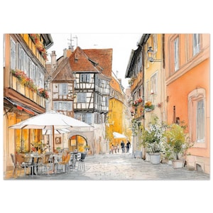 May include: Watercolor painting of a European street scene. Buildings with orange tile roofs and timber-framed walls line a cobblestone street. A white umbrella shades a cafe with tables and chairs. Flowers and plants add color.