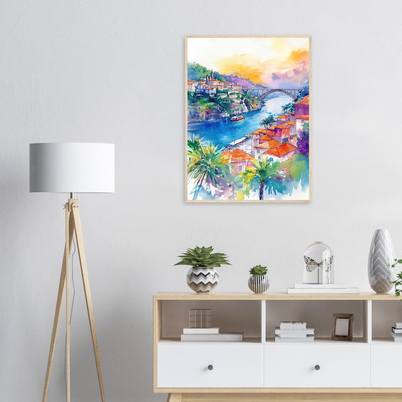 Op de afbeelding: Aquarel schilderij van een kustplaats met rode pannendaken, palmbomen en een brug over een blauwe rivier. De lucht gaat over van oranje naar geel, waardoor een levendig en kleurrijk landschap ontstaat. Het kunstwerk is ingelijst.