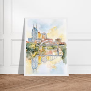 Puede incluir: Pintura a la acuarela del horizonte de Nashville, con el ic&oacute;nico edificio AT&T y un puente sobre el r&iacute;o Cumberland. La obra de arte tiene una paleta de colores pastel suaves con reflejos en el agua. La obra se muestra sobre un fondo blanco.