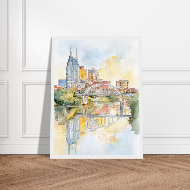 Puede incluir: Pintura a la acuarela del horizonte de Nashville, con el ic&oacute;nico edificio AT&T y un puente sobre el r&iacute;o Cumberland. La obra de arte tiene una paleta de colores pastel suaves con reflejos en el agua. La obra se muestra sobre un fondo blanco.