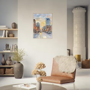 May include: A framed watercolor painting depicting a city street scene at sunset with tall buildings, glowing streetlights, and a golden sky. The artwork features a perspective view of a bustling urban road with warm orange and cool blue tones.