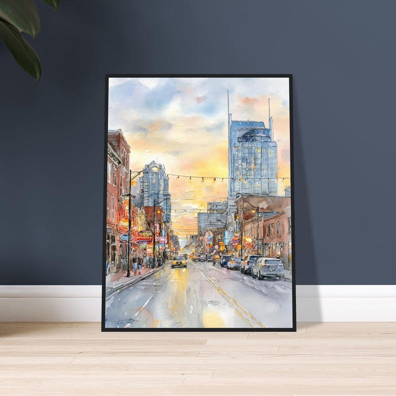 May include: A framed watercolor painting depicting a city street scene at sunset. The composition features tall buildings, glowing street lights, and vehicles on a road. The sky is filled with warm yellow and orange hues, contrasting with the cool blue tones of the architecture and the street level, creating a vibrant urban atmosphere.