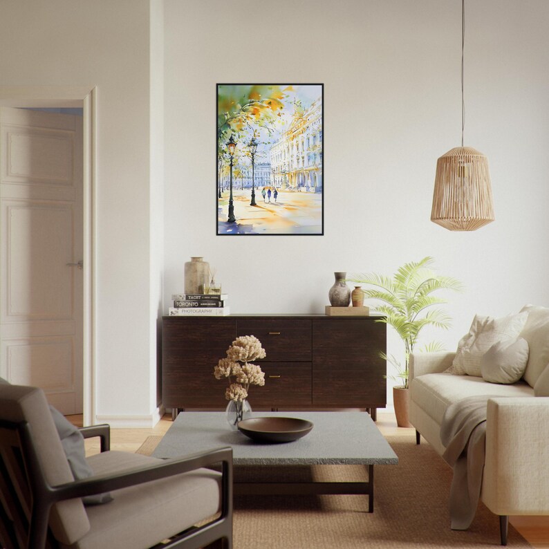 Op de afbeelding: Een aquarel schilderij van een stadstraat sc&egrave;ne met gebouwen, bomen en mensen die lopen. Het schilderij is ingelijst in een zwart frame en hangt aan een witte muur.