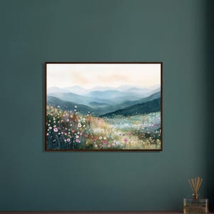 May include: A framed landscape wall art print featuring a watercolor painting of a mountain range in soft blue and grey tones, overlooking a vibrant meadow filled with small pink, white, and yellow wildflowers under a pale sky.