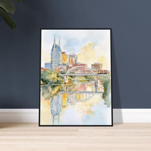 Puede incluir: Pintura a la acuarela de un paisaje urbano con un puente sobre un r&iacute;o. Los edificios son en tonos dorados, azules y marrones. El puente es blanco con detalles rojos. La pintura est&aacute; enmarcada en un marco negro.