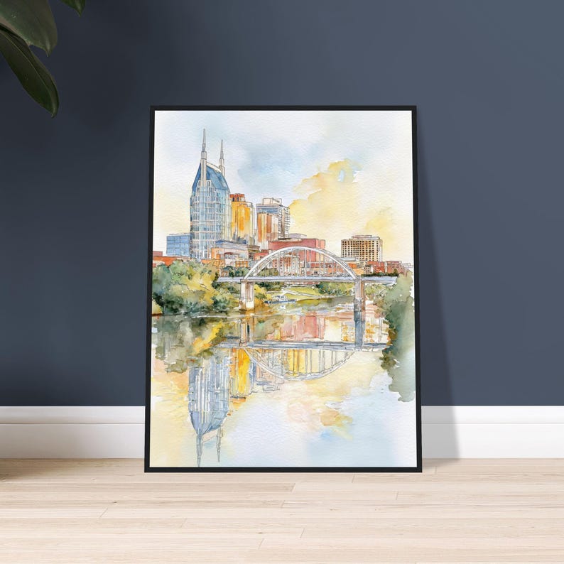 Puede incluir: Pintura a la acuarela de un paisaje urbano con un puente sobre un r&iacute;o. Los edificios son en tonos dorados, azules y marrones. El puente es blanco con detalles rojos. La pintura est&aacute; enmarcada en un marco negro.