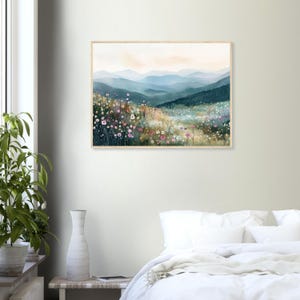 May include: A rectangular wall art print in a light wood frame featuring a landscape painting of rolling blue mountains in the distance behind a foreground filled with colorful wildflowers in shades of pink, white, and yellow.