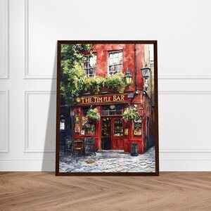 May include: A framed painting of The Temple Bar, featuring a vibrant red facade with gold lettering, large windows, and lush green foliage hanging above the entrance. The scene includes a cobblestone street, a dark trash bin, and wall signs.