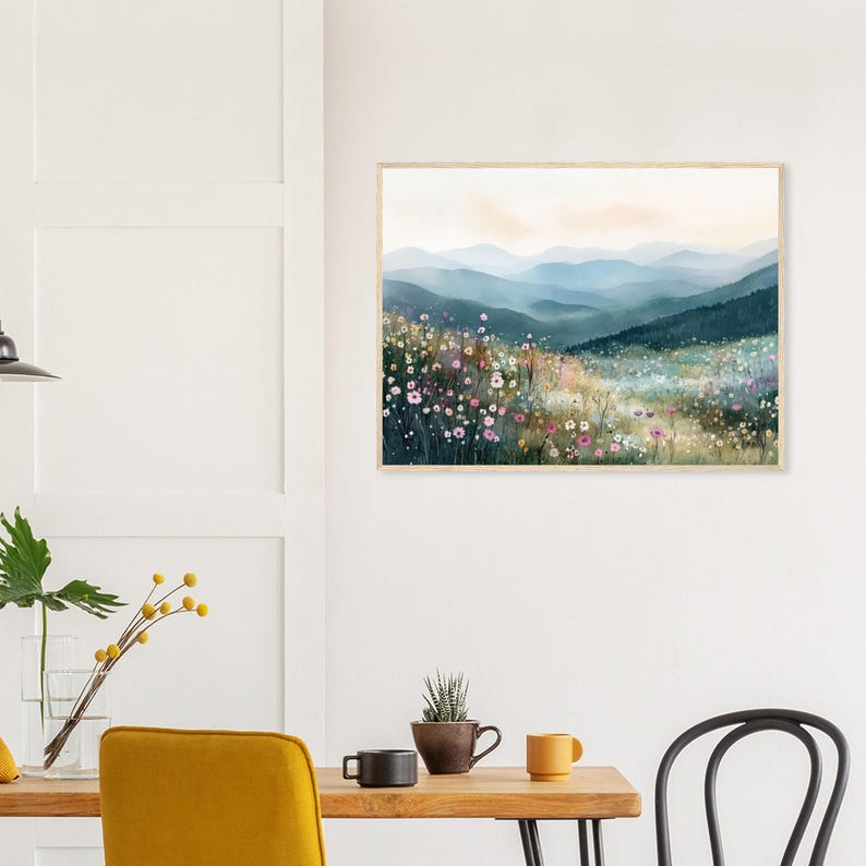 May include: A rectangular wall art print in a light wood frame featuring a watercolor landscape painting of rolling blue mountains in the distance behind a foreground filled with colorful wildflowers in shades of pink, white, and yellow.