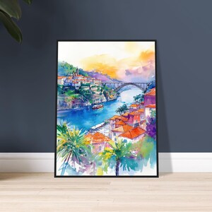 Op de afbeelding: Aquarel schilderij van een Europese stadsgezicht met een brug over een rivier. Het kunstwerk toont gebouwen met oranje daken, palmbomen en een levendige lucht met tinten oranje, geel en paars. De schilderij is ingelijst in een zwart frame.