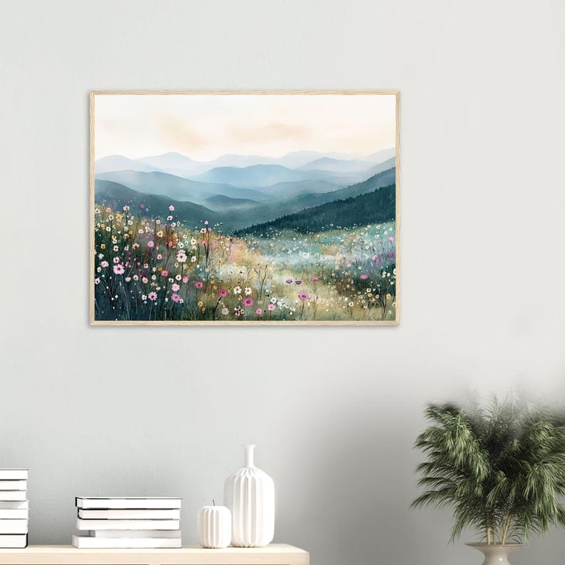 May include: A rectangular wall art print featuring a landscape painting of a wildflower meadow in the foreground with pink, white, and yellow blossoms. In the background, layers of blue and green mountains fade into a soft sky.