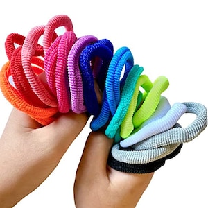 Puede incluir: Un conjunto de gomas para el pelo de colores en un arco&iacute;ris de colores, incluyendo naranja, rosa, morado, azul, verde, amarillo, blanco, gris y negro.
