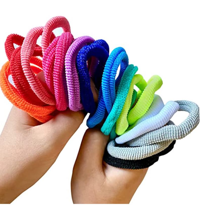 Puede incluir: Un conjunto de gomas para el pelo de colores en un arco&iacute;ris de colores, incluyendo naranja, rosa, morado, azul, verde, amarillo, blanco, gris y negro.