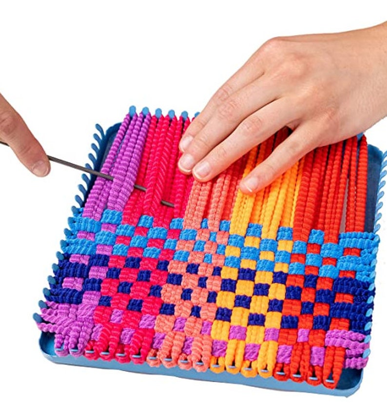 Puede incluir: Un telar de pl&aacute;stico azul con hilo de colores tejido en un patr&oacute;n de cuadros. El telar se est&aacute; utilizando para crear un proyecto tejido de colores.