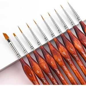May include: Set of 10 fine tipped paint brushes with wooden handles. The brushes are numbered 0, 1, 2, 3, 4, 5, 6, 7, 8, and 10. The brushes are arranged in order of size, with the smallest brush on the left and the largest brush on the right.