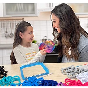 Puede incluir: Una ni&ntilde;a y una mujer est&aacute;n sentadas en una mesa haciendo pulseras de loom arco&iacute;ris. Est&aacute;n usando un telar y gomas el&aacute;sticas de colores. El telar es azul y tiene forma cuadrada. Hay muchas gomas el&aacute;sticas de colores en la mesa.