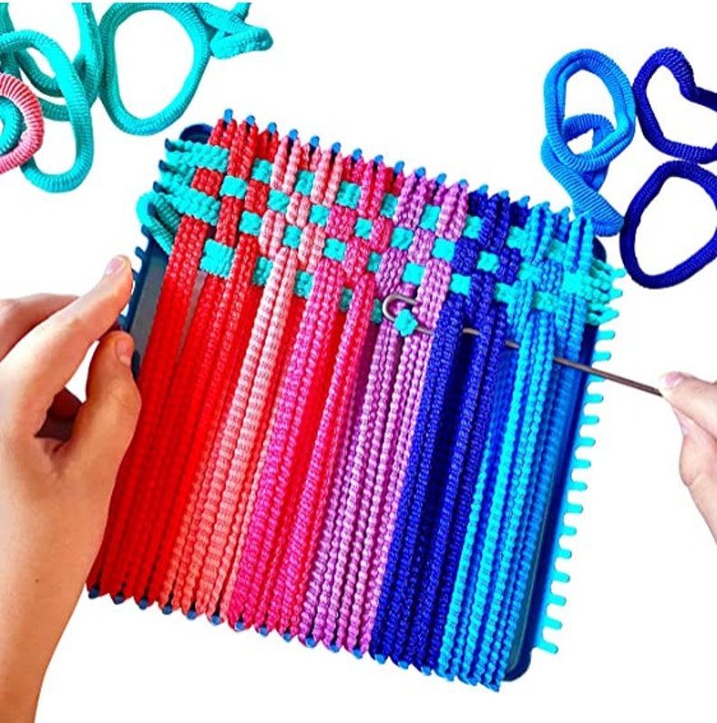 Puede incluir: Un telar de pl&aacute;stico azul con gomas el&aacute;sticas de colores tejidos en un patr&oacute;n. Se utiliza un gancho y una aguja de metal para tejer las gomas.