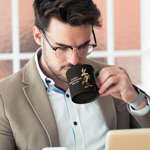 A black coffee mug with a cartoon Wile E Coyote in brown and tan colors. The coyote is standing with its right paw raised. The text on the mug reads 'Under-appreciated Genius'.