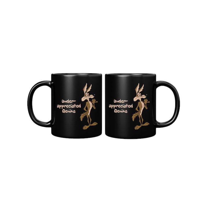 A black coffee mug with a cartoon Wile E Coyote in brown and tan colors. The coyote is standing with its right paw raised. The text on the mug reads 'Under-appreciated Genius'.