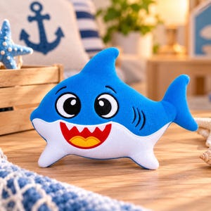 May include: A plush shark toy featuring a bright blue upper body and a white underbelly. The shark has large black and white eyes, a wide open mouth with white teeth, a red interior, and a yellow tongue. It has a dorsal fin and side fins.