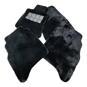 Puede incluir: Juego de cuatro alfombrillas negras para coche. Las alfombrillas están hechas de un material afelpado y peludo. Una alfombrilla tiene un parche rectangular con un diseño acolchado. Las alfombrillas protegen el interior del coche.