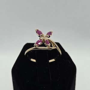 May include: A gold ring with a delicate design featuring five red ruby stones set in a butterfly shape.