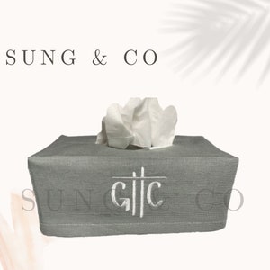 Könnte beinhalten: Graue Leinen-Tischtuchbox mit weißen gestickten Initialen "G.T.C."