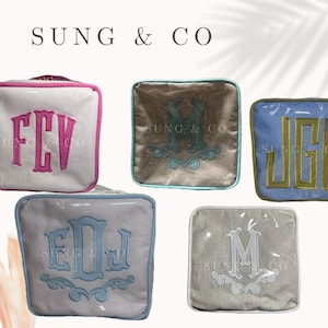 May include: Five cosmetic bags with different monogram initials. The bags are made of a soft, textured fabric and have a clear plastic top. The initials are embroidered in different colors on each bag. The bags are all lined up in a row on a white background.