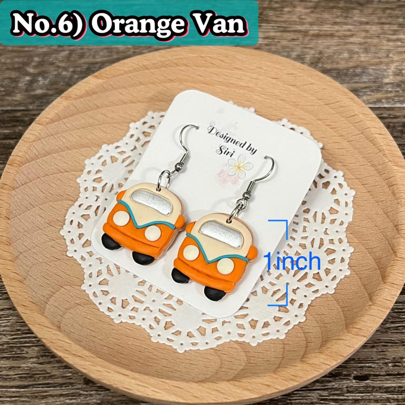 May include: Orange van earrings with silver hooks, approximately 1 inch in length. The earrings are orange, cream, and black, with a turquoise accent. The earrings are displayed on a white card with the text "Designed by Siri". The text "No.6) Orange Van" is at the top.