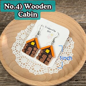 May include: A pair of dangle earrings shaped like miniature wooden cabins. The cabins are brown with orange roofs and yellow windows. The earrings are approximately 1 inch in length and hang from silver-colored hooks. The text "No.4) Wooden Cabin" is visible.