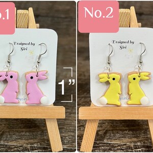 May include: Two pairs of polymer clay bunny earrings. The first pair is pink and the second pair is yellow. Each pair is 1 inch long. The earrings are on a white card with the text "Designed by Siri" and "@bysiri".